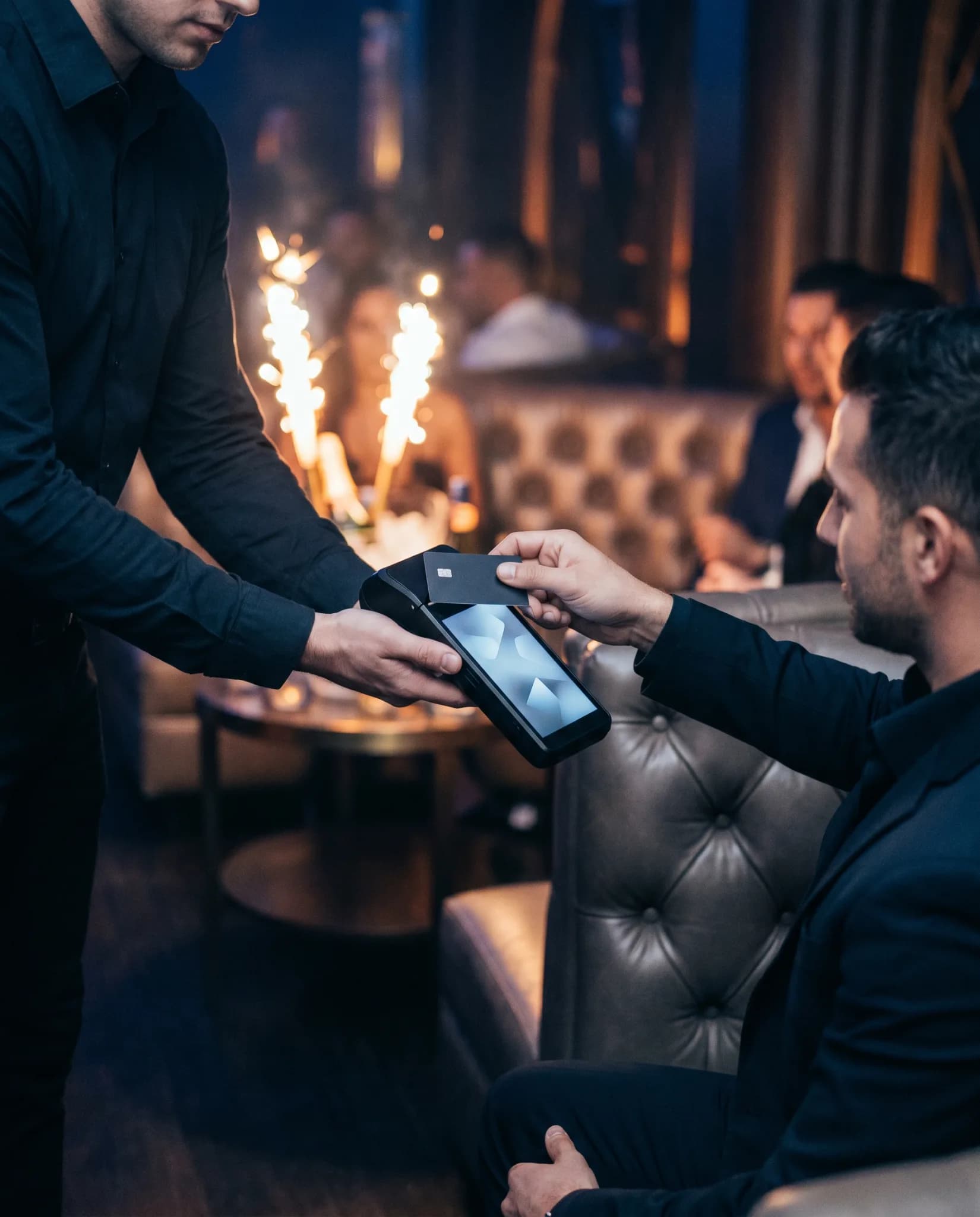 A guest tapping a card on a handheld terminal in a dark venue